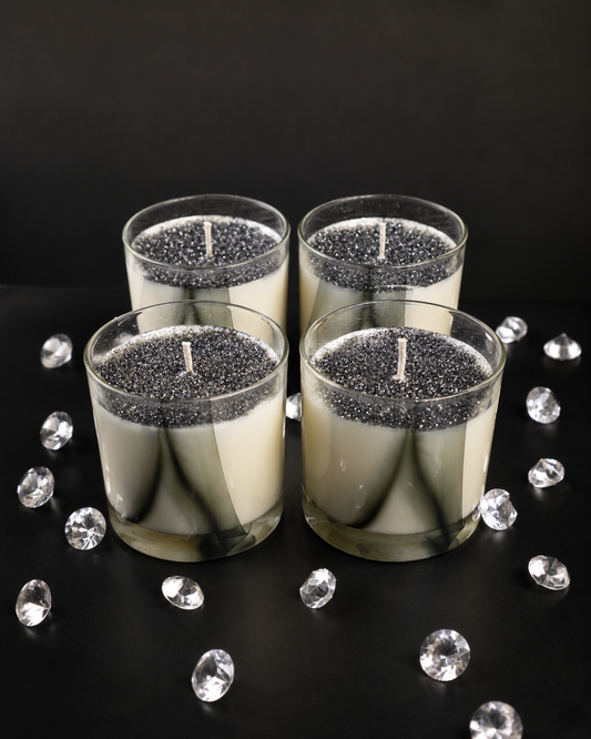 Four glass candles with glittery bases on a black surface with decorative crystals.