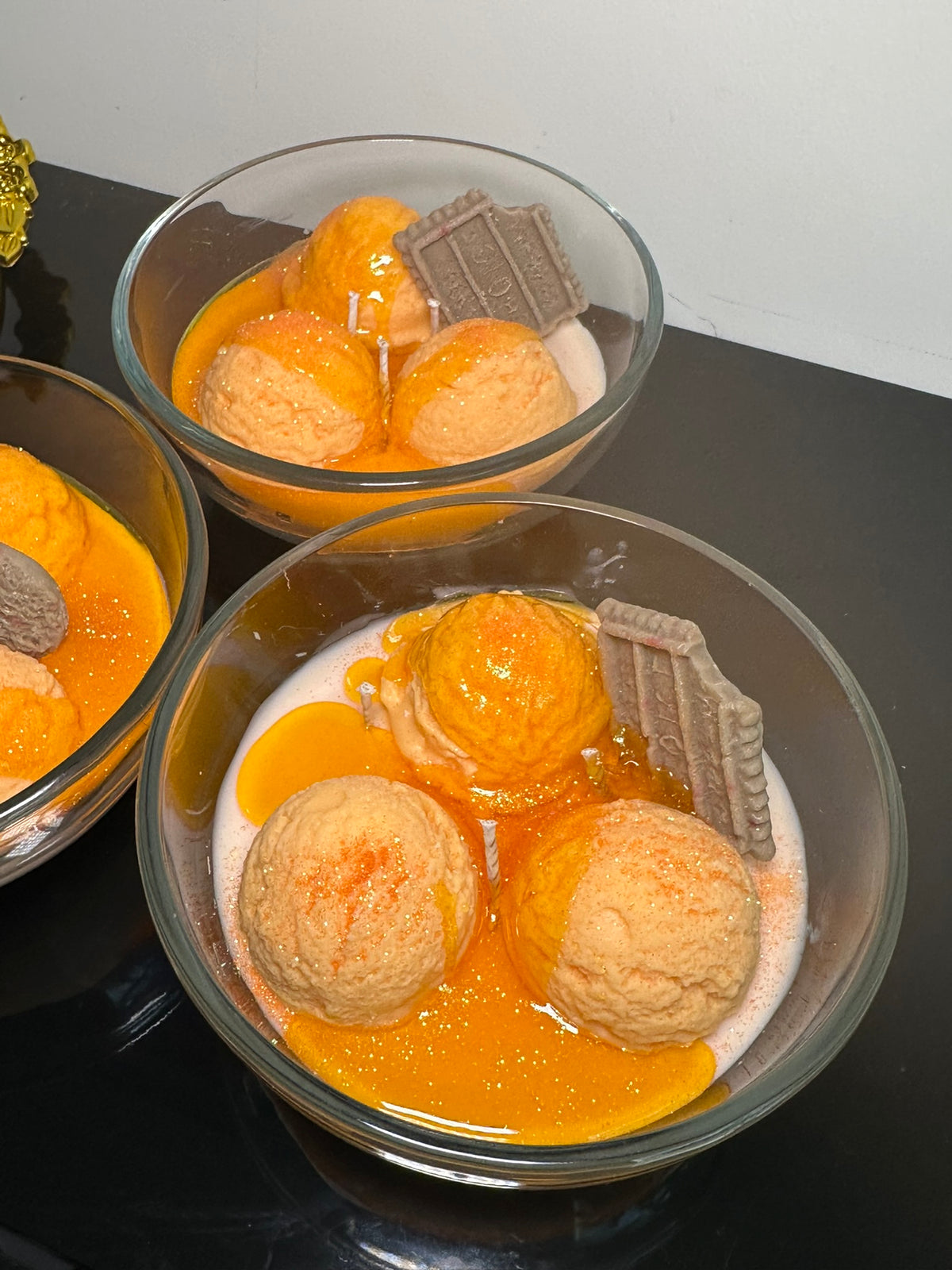 Two glass bowls of orange ice cream made with soy wax sitting on a dark surface