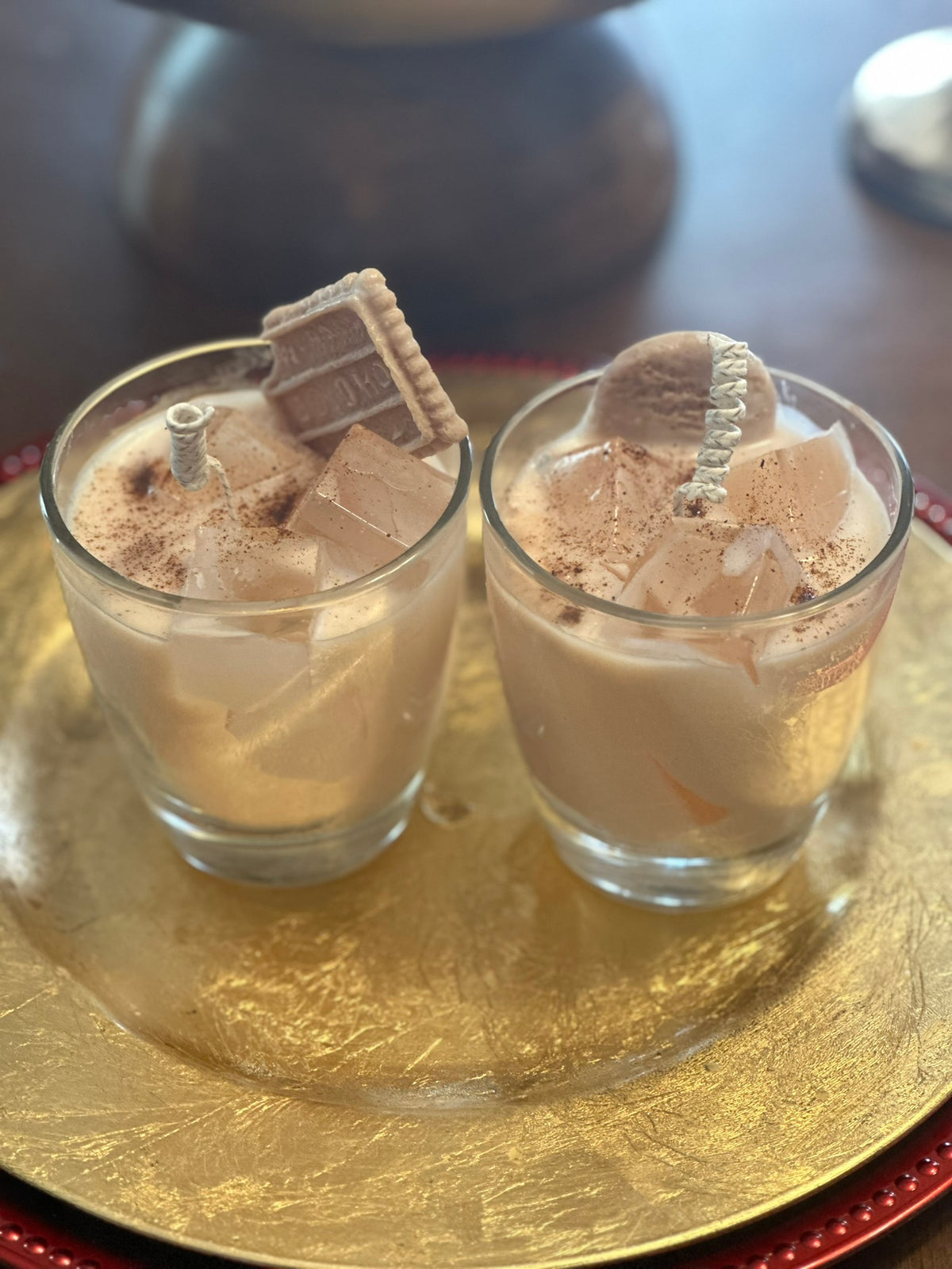 Two glasses of a egg nog made with soy and gel wax, topped with biscoff cookies sitting on a gold tray.