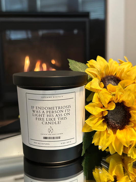 Candle with a humorous label next to sunflowers in front of a fireplace
