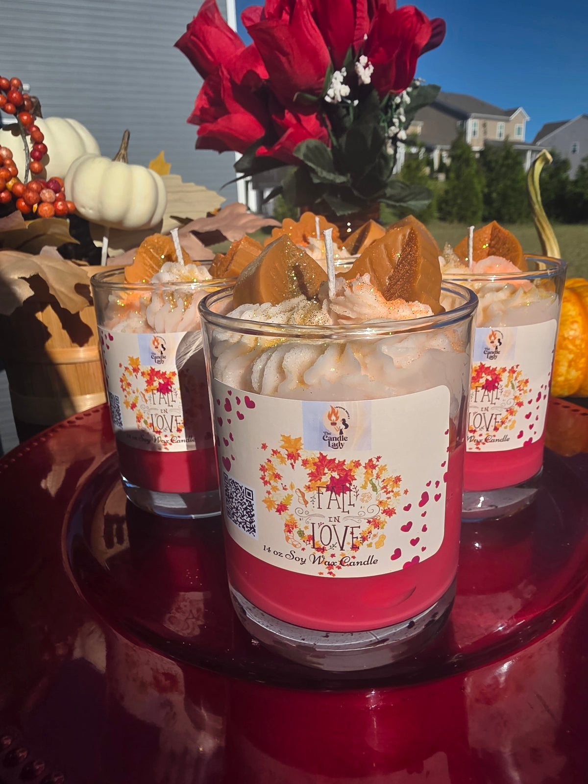 Three candles with fall-themed labels on a red surface outdoors.