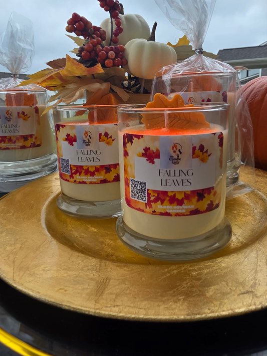 Candle with 'Falling Leaves' label on a wooden surface with pumpkins and leaves in the background.