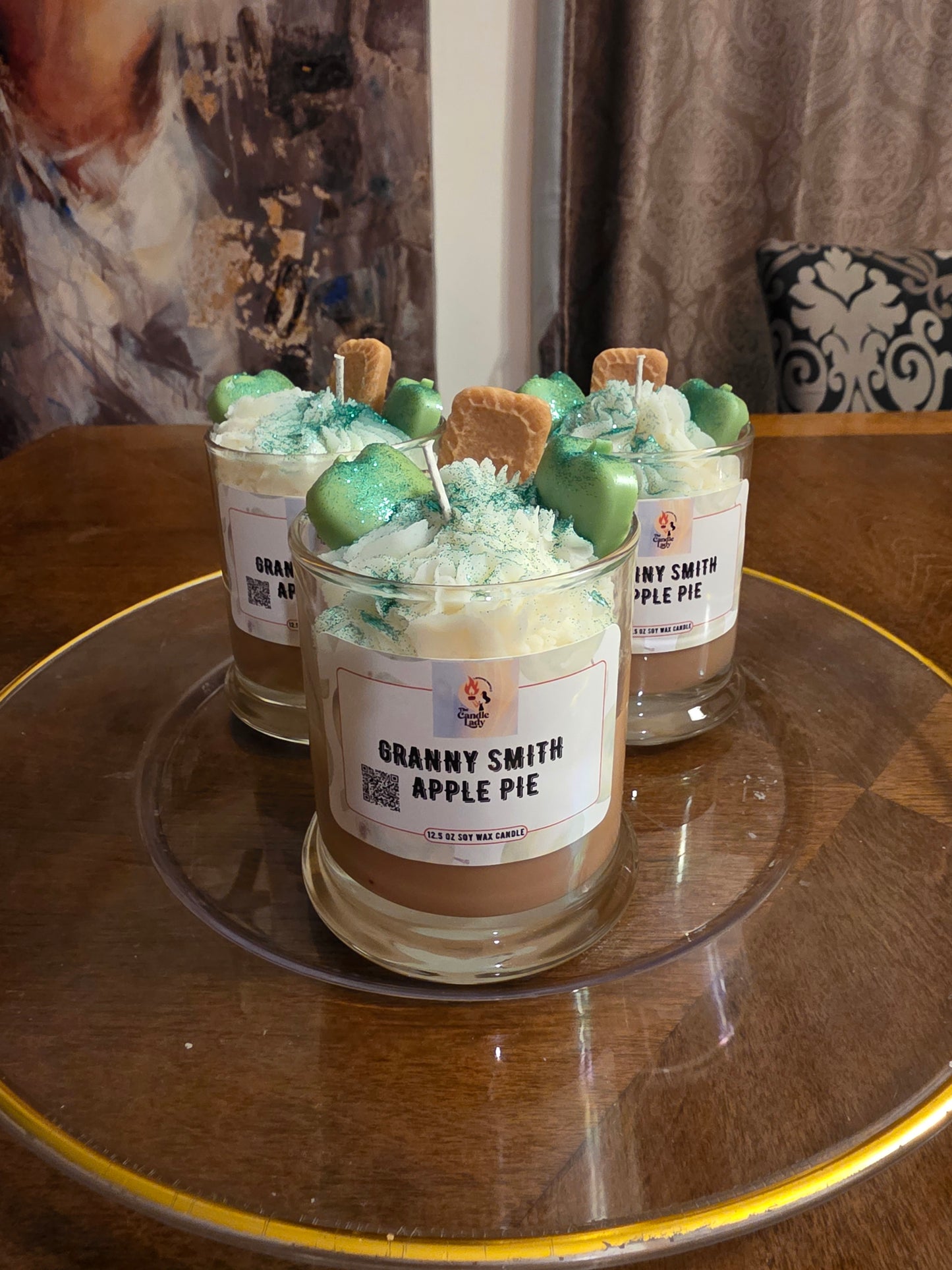 Two jars of Granny Smith Apple Pie Candle on a glass table with a blurred background