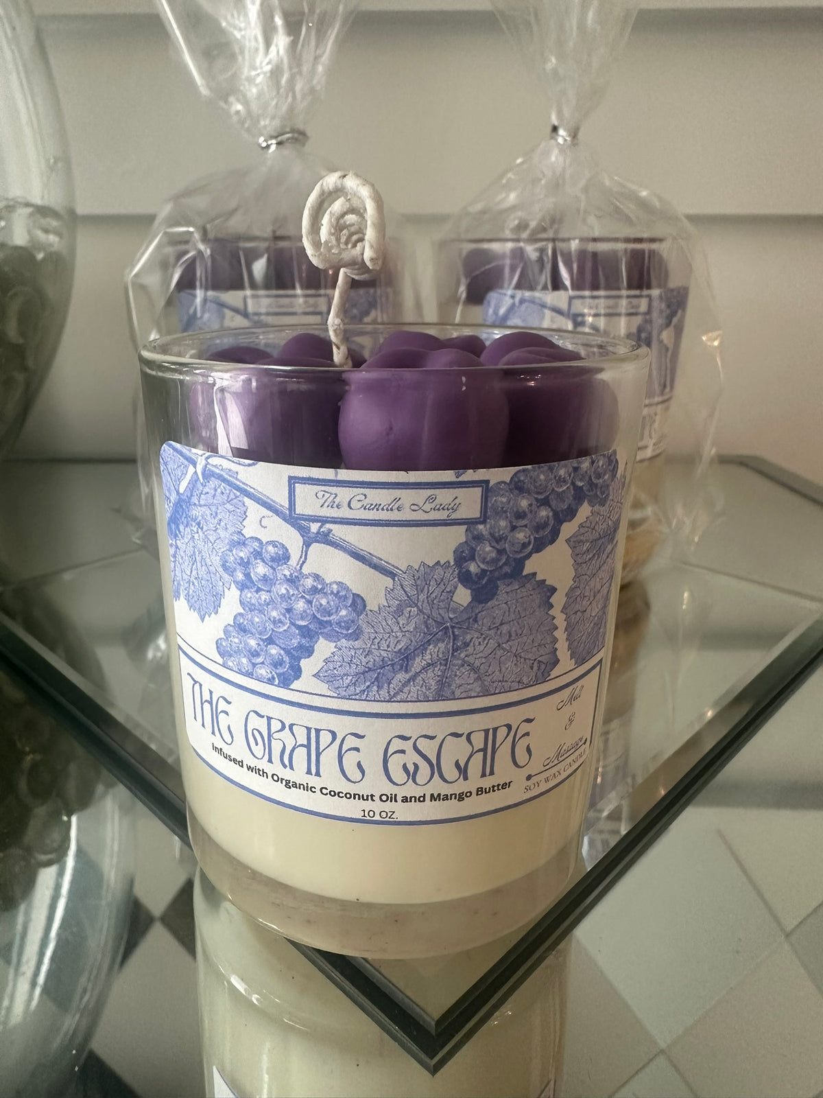Candle labeled 'The Grape Escape' on a glass surface with a blurred background