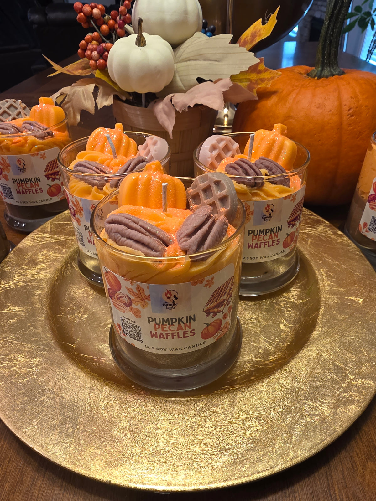 Pumpkin-themed candles on a gold tray with decorative pumpkins and leaves in the background.