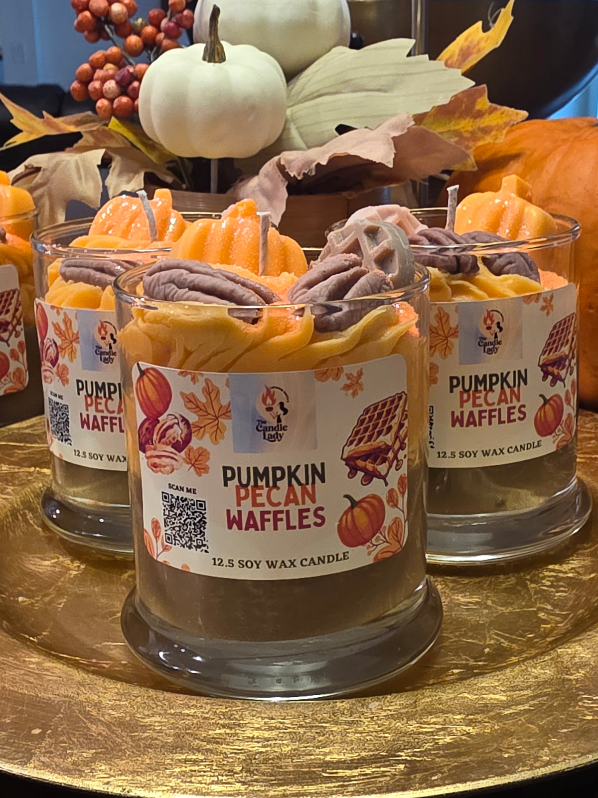 Two jars of 'Pumpkin Pecan Waffles' candle on a decorative stand with pumpkins and leaves.