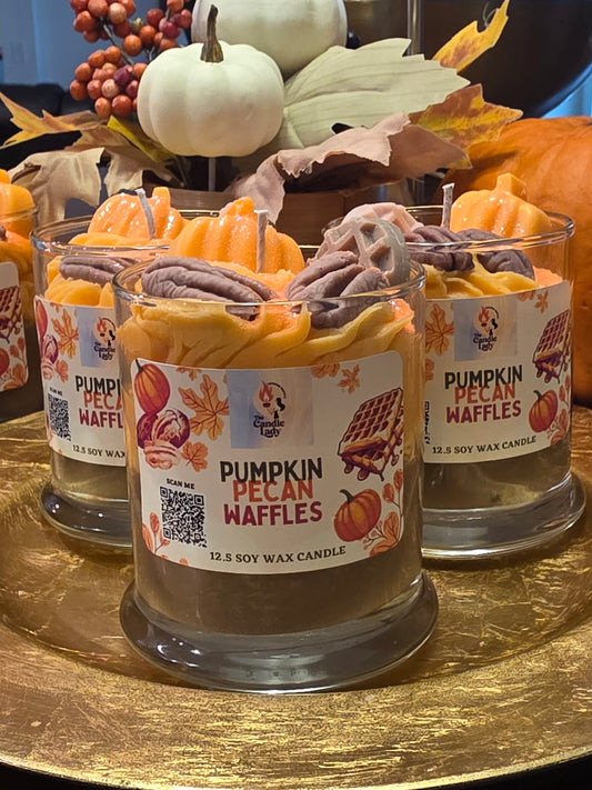 Two jars of 'Pumpkin Pecan Waffles' candle on a decorative stand with pumpkins and leaves.