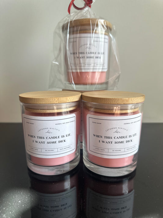 Three candles with clear glass jars and wooden lids, two with labels and one wrapped in a transparent bag with a label. The labels have text related to the product's branding and scent.