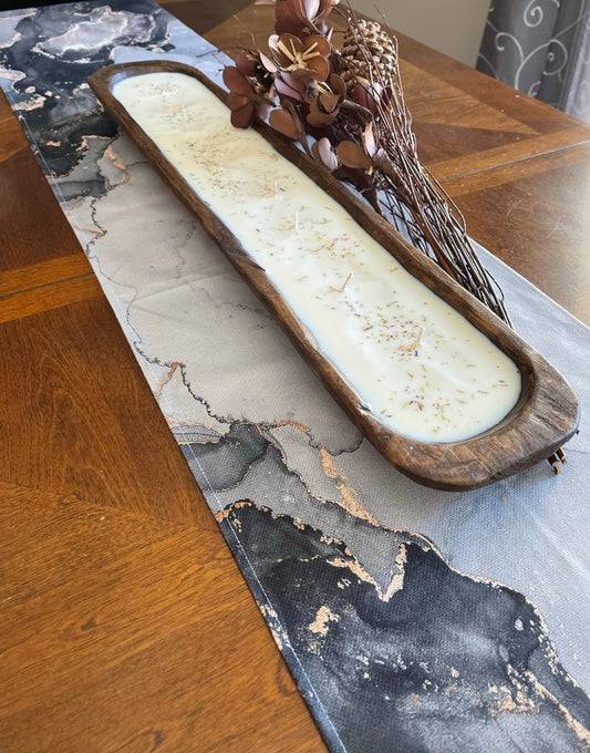 Decorative 36' dough bowl candle in a wooden holder on a marble-patterned table runner.